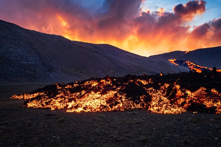 A volcanic gas cloud blooms over a river of lava in Iceland